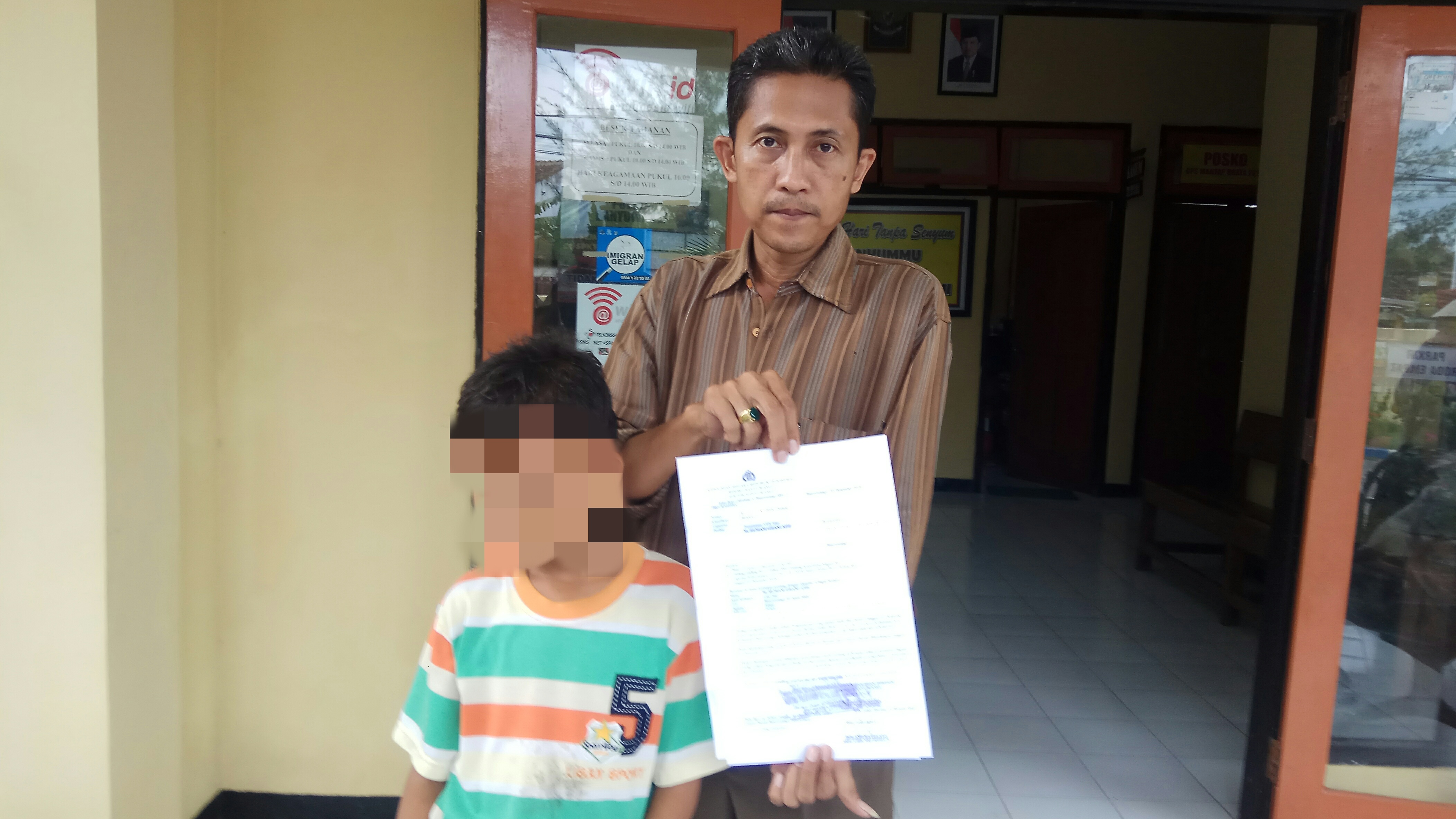 Slamet bersama anaknya menunjukkan pengantar visum usai melapor di Polsek Banyuwangi