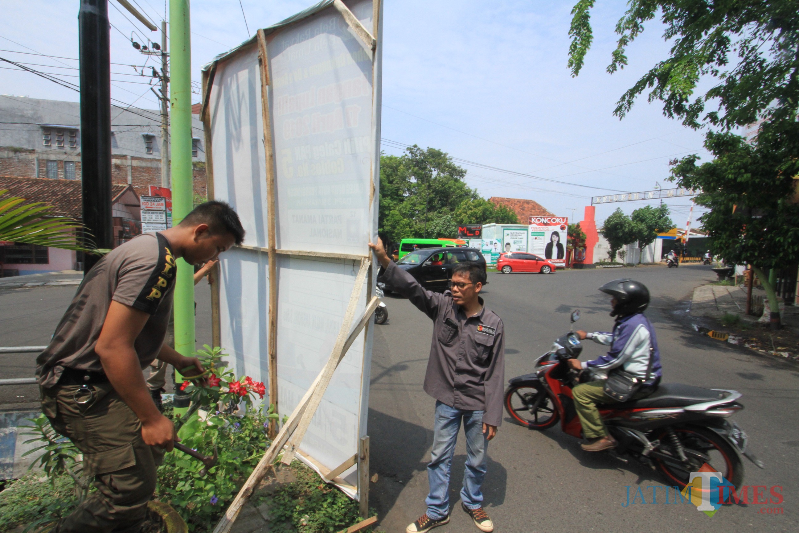 Petugas menurunkan APK Caleg yang menghalangi pandangan pengendara di perempatan jalan KH Mansur (Agus Salam/JatimTIMES)