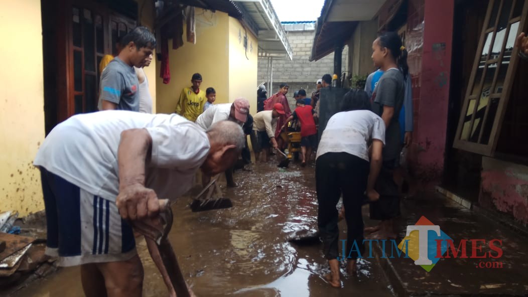Warga membersihkan material lumpur yang terbawa luapan air sungai