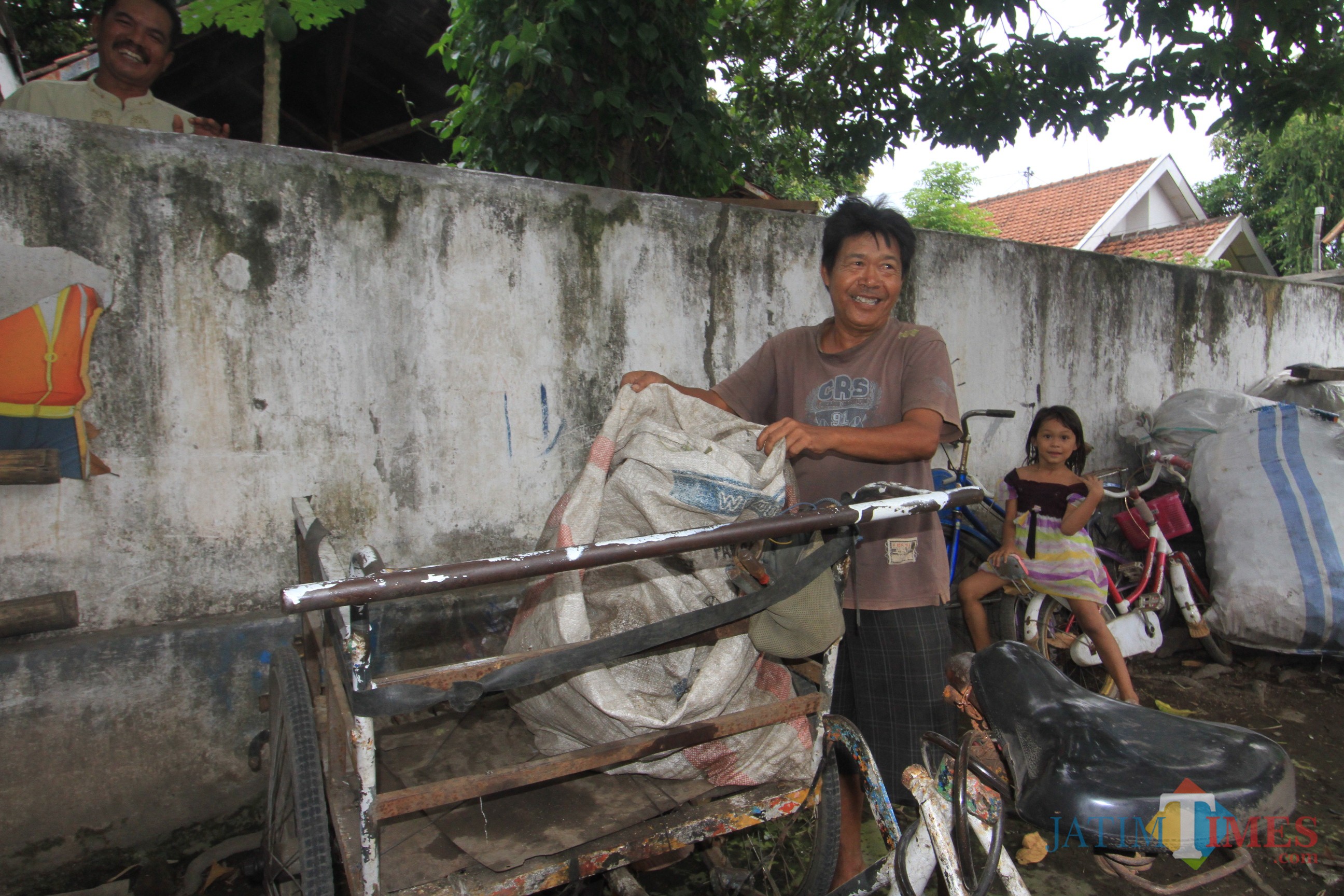 Hari Libur saat menurunkan rongsokan dari becaknya (Agus Salam/Jatim TIMES)