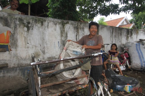 Hari Libur saat menurunkan rongsokan dari becaknya (Agus Salam/Jatim TIMES)