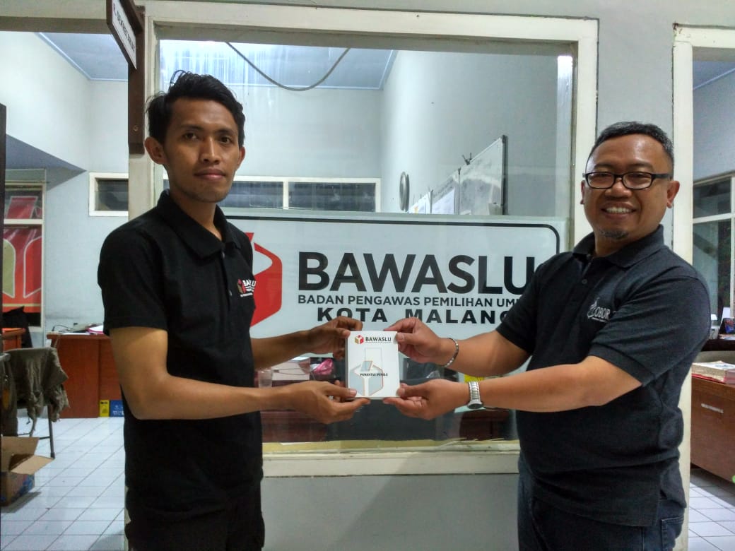 Muhammad Faris Abdul Aziz dari Bawaslu Jatim menyerahkan Kartu Identitas Pemantau kepada Felik Sad Windu selaku koordinator pemantau dari Ma Chung. (Foto: Humas)