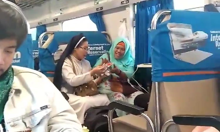 Seorang suster membagikan makanan ringan kepada seornag wanita muslim di atas kereta. (Foto: video @rfxzpt)