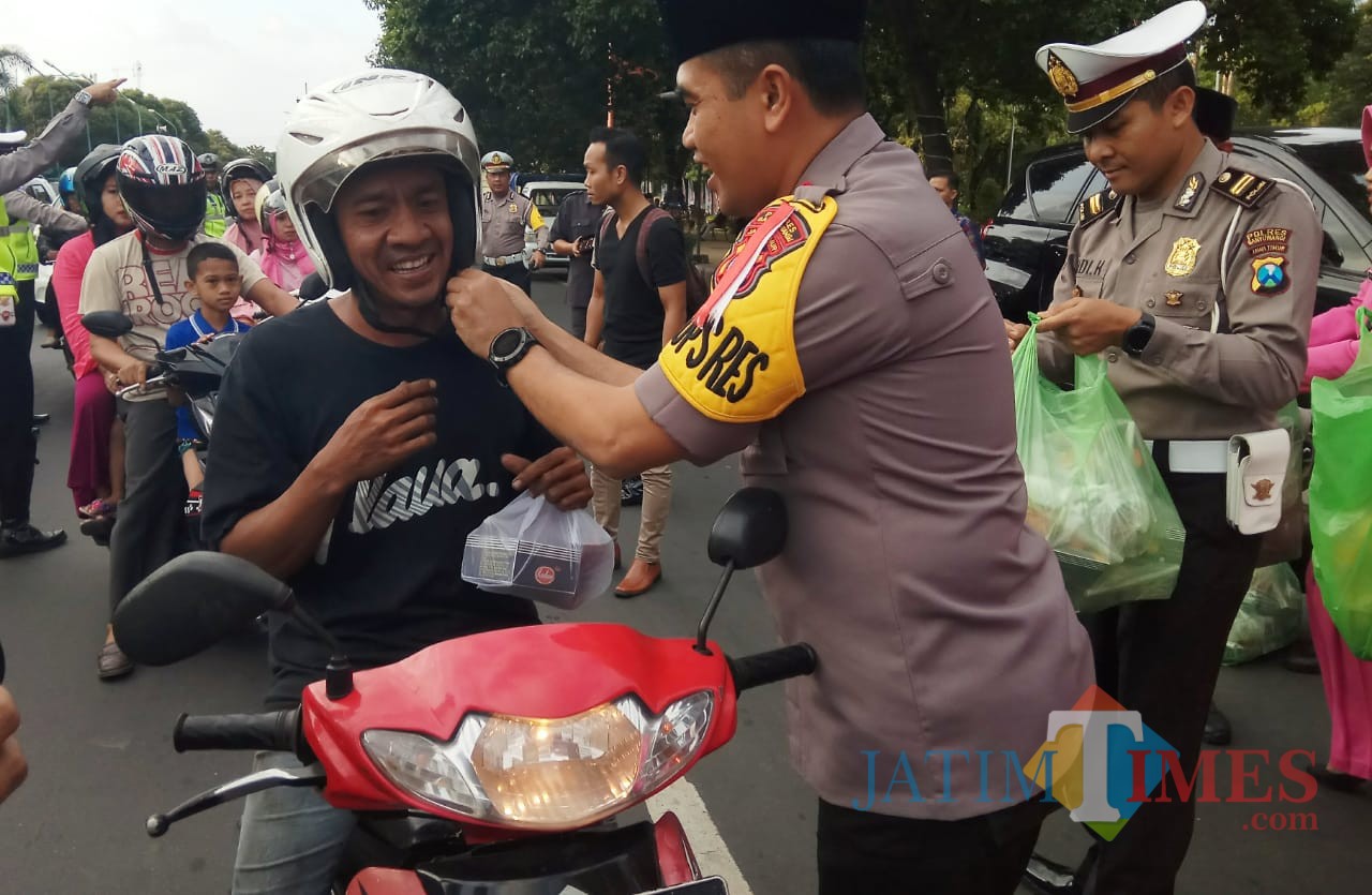 Kapolres Banyuwangi AKBP Taufik HZ memasangkan tali pengaman helm pengendara motor disela pembagian takjil gratis
