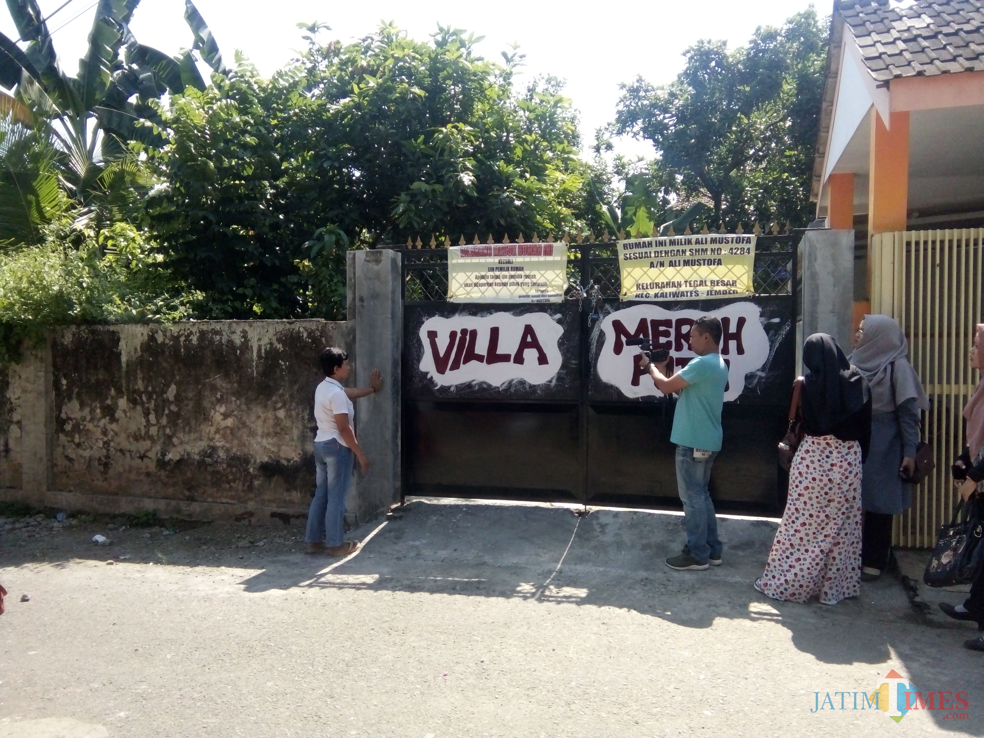Senema (kiri berkaos putih) saat menunjukkan gerbang yang menuju akses rumahnya dalam kondisi terkunci (foto : Moh. Ali Makrus / JatimTIMES)
