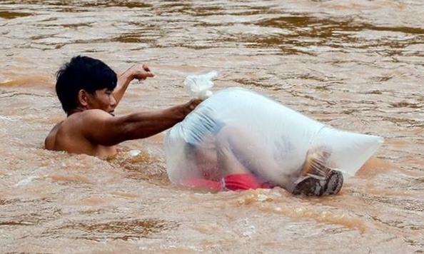 Seorang pria saat menyeberangkan anak dalam plastik di sebuah sungai. (Foto: istimewa)