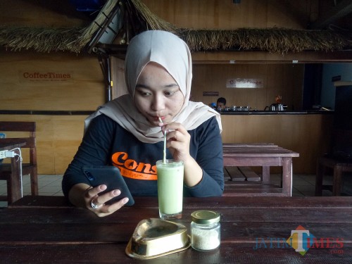 Pelanggan Coffee Times, Lisdya Shelly, sedang asyik bekerja sambil menikmati green tea Coffee Times. (Foto: Imarotul Izzah/MalangTIMES)