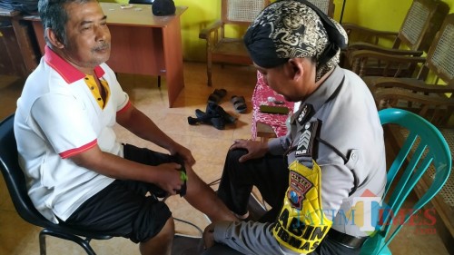 Bripka Agus Budiono saat mengobati salah satu pasien. (Eko Arif S /JatimTIMES)