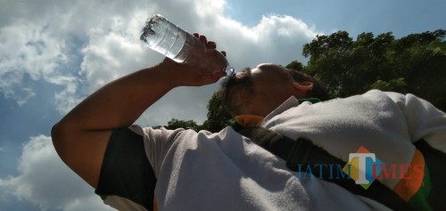 Salah satu warga minum air untuk mengurangi dehidrasi dari efek Kulminasi (foto: Joko Pramono/JatimTIMES)