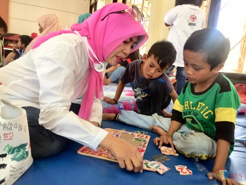Salah satu anak yang mengungsi asyik bermain didampingi relawan di posko Balai Desa Punten, Senin (21/10/2019). (Foto: Irsya Richa/MalangTIMES)
