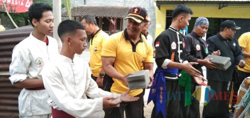 Kapolsek Kota, Kompol Rudi Purwanto mengangkut material bedah rumah bersama anggota perguruan silat (foto: Joko Pramono/ Jatim Times)