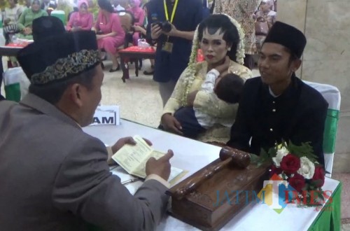 Salah satu pasangan pengantin yang mengikuti nikah masal saat prosesi akad nikah sambil menggendong anak (Arifina Cahyanti Firdausi/MalangTIMES)