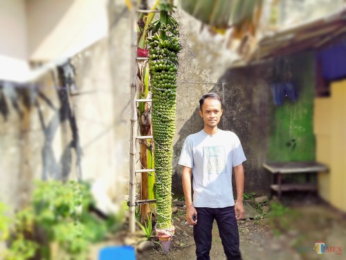 Titor bersama pohon pisang di samping rumahnya yang berbuah tak seperti umumnya pisang. (Anggara Sudiongko/MalangTIMES)