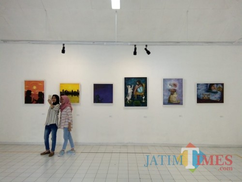 Pengunjung pameran tengah berfoto di depan lukisan hasil karya mahasiswa Universitas Negeri Malang di Gedung Dewan Kesenian Malang (Pipit Anggraeni)