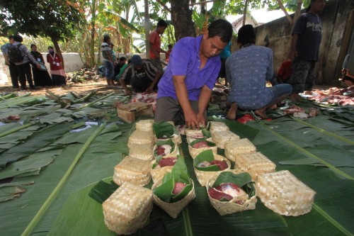 Salah satu panitia kurban membungkus daging kurban dengan besek yang dilapisi daun pisang (Agus Salam/Jatim TIMES)