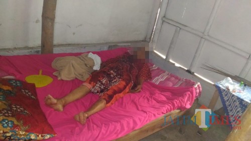 Korban saat pertama ditemukan tetangganya di tempat tidur dalam kondisi luka di leher. (foto : istimewa / Jatim TIMES)