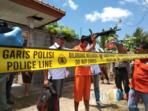 pelaku nando saat memperagakan adegan membuang senapanyang digunakan untuk membunuh korban ke kebun di belakang rumah korban. (foto : Joko Pramono/jatim Times)