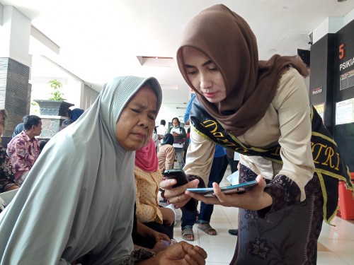 Duta bSi Poetri mengajarkan pada pasien untuk mendaftar menggunakan gawainya (Joko Pramono for JatimTIMES)