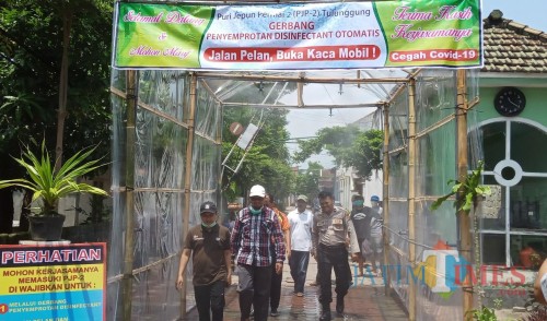 Warga melewati lorong Disinfektan di perumahan PJP 2 (Joko Pramono for Jatim Times)