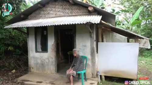Kondisi Mbah Ginten yang sedang duduk di depan rumahnya, yang berada di pelosok perkampungan Desa Pakem, Kecamatan Wajak, Kabupaten Malang. (Foto: YouTube Cak Budi Official)