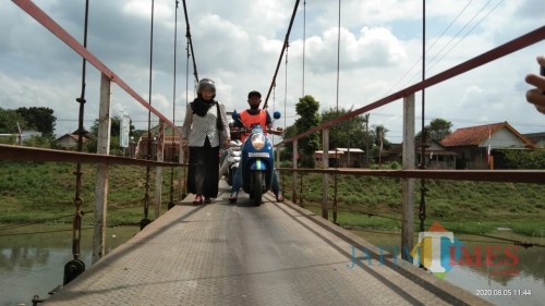 Salah satu warga yang takut melintas di jembatan gantung dibantu oleh penjaga jembatan (Joko Pramono for Jatim TIMES)