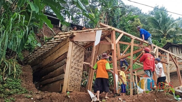 Petugas bersama warga ketika membenahi rumah warga yang terkena longsor. (Foto: Bams Setioko/JatimTIMES)