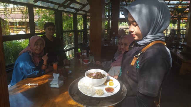 Salah satu pramusaji NK Cafe Malang menyajikan rawon untuk pengunjung. (Foto: Nurlayla Ratri/Jatimtimes)