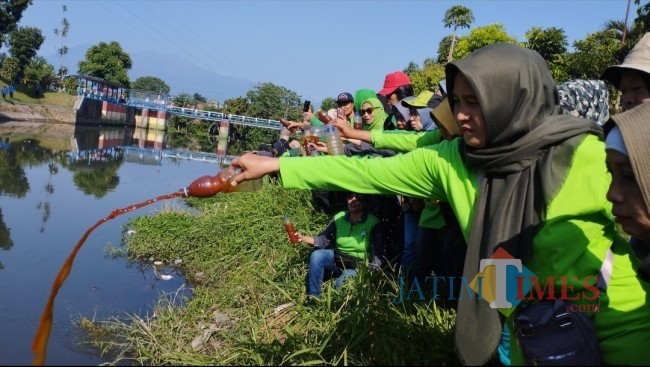 Peserta kerja bakti dari Kader Lingkungan saat menyiramkan air enzim pada Sungai Rolak agar kembali jernih (foto: Hendra Saputra/JatimTIMES)