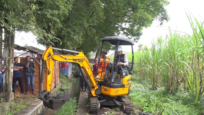 Pj Wali Kota Malang Wahyu Hidayat menjajal eskavator untuk membangun irigasi petani.(Foto: Ahmad Amin/MalangTIMES).